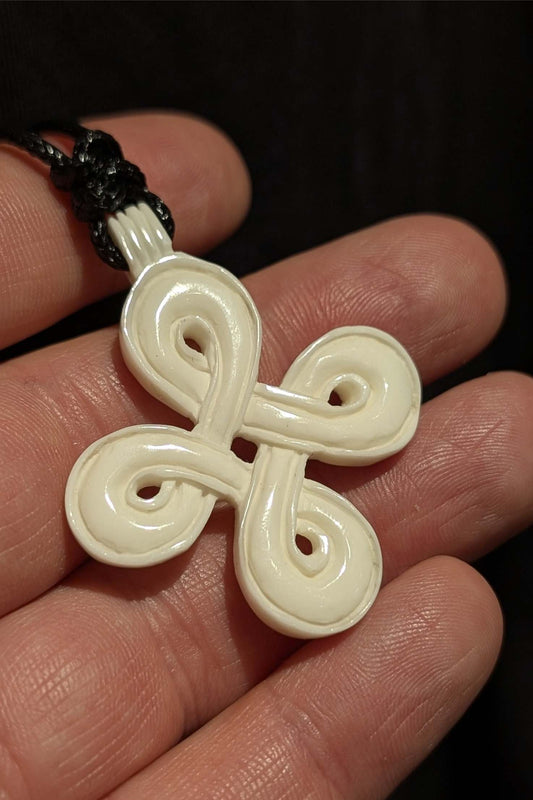 White Celtic knot pendant held between fingers against a dark background
