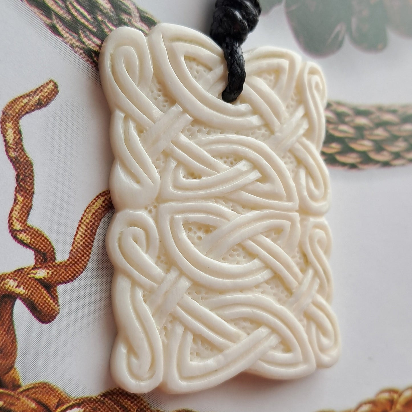 Bone Celtic woven pendant with braided cords on a white background